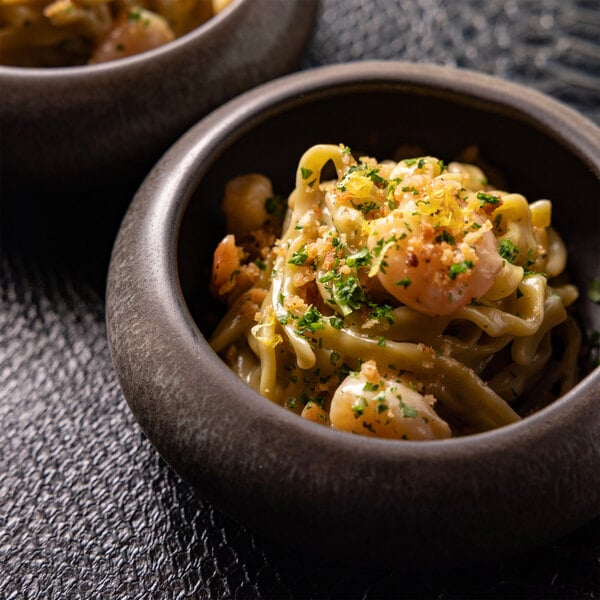 A round stoneware bowl filled with pasta, shrimp, and garnished with herbs.