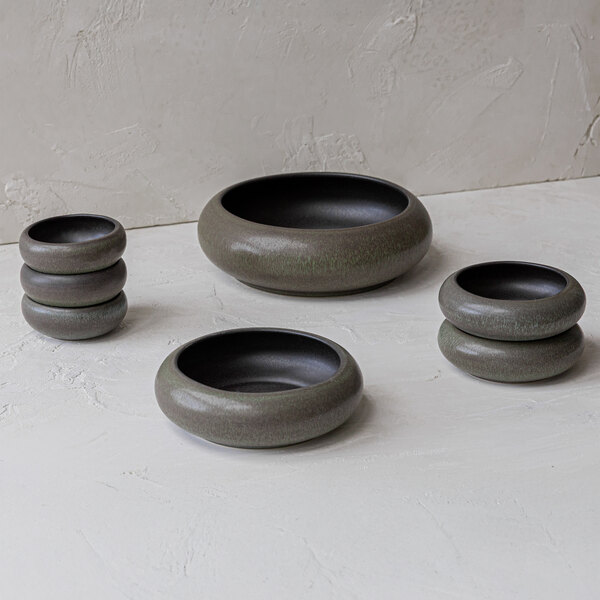 Four round, greenish-brown stoneware bowls of varying sizes are arranged on a light textured surface.