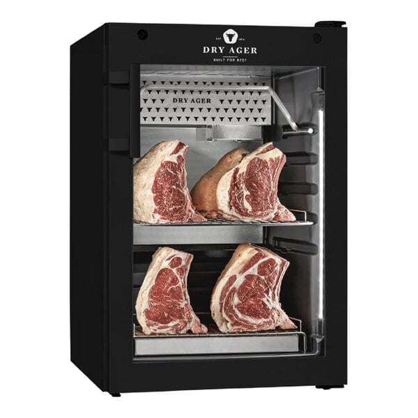 A black meat curing cabinet with glass door containing several large cuts of beef.