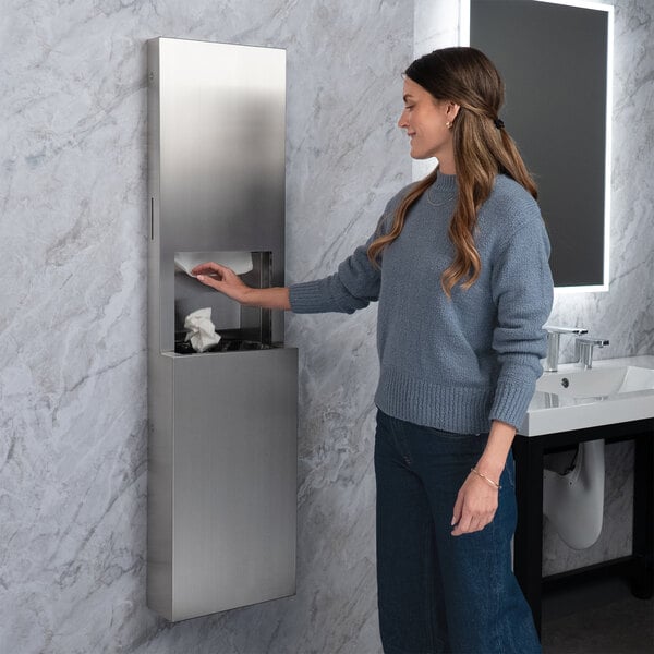 A stainless steel surface-mounted paper towel dispenser and waste receptacle with a satin finish, installed on a restroom wall.