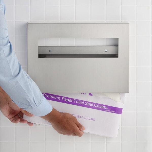 A stainless steel surface-mounted toilet seat cover dispenser being refilled with paper seat covers.