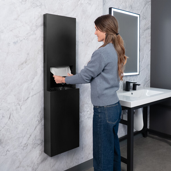 A matte black surface-mounted paper towel dispenser and waste receptacle installed on a restroom wall.