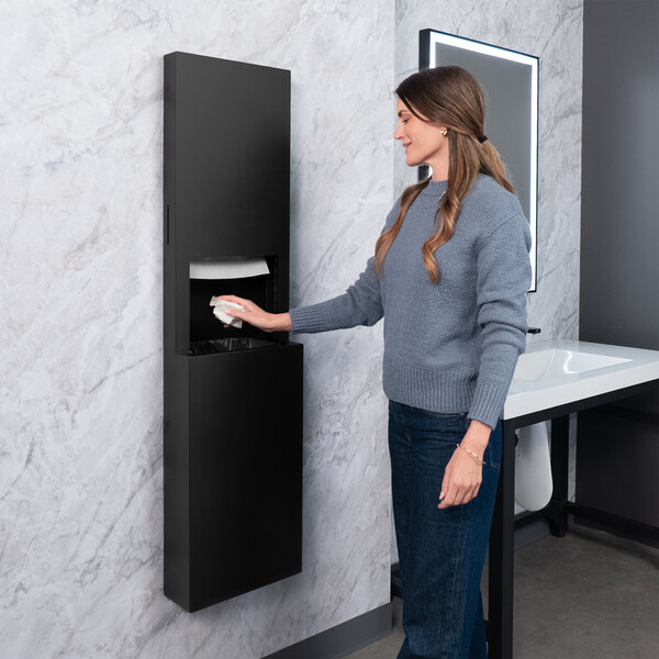 A matte black surface-mounted paper towel dispenser and waste receptacle installed on a restroom wall.