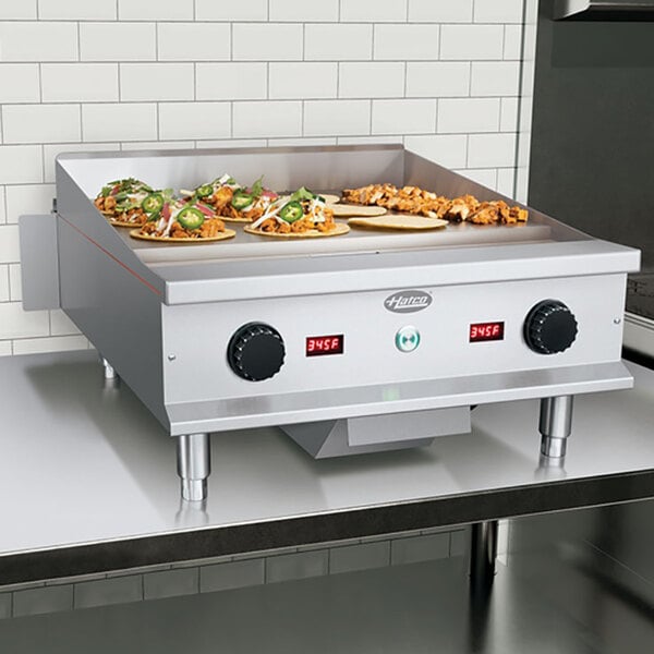 A stainless steel 24-inch countertop induction griddle with digital temperature displays and food cooking on the surface.