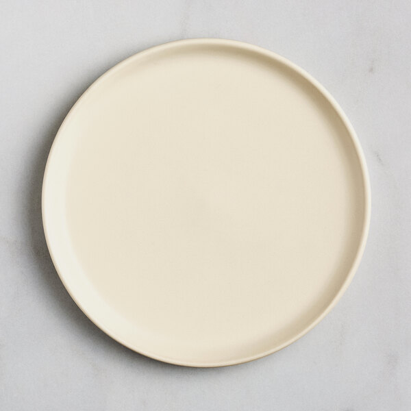 A round, off-white plate with a smooth matte finish, viewed from above on a light surface.