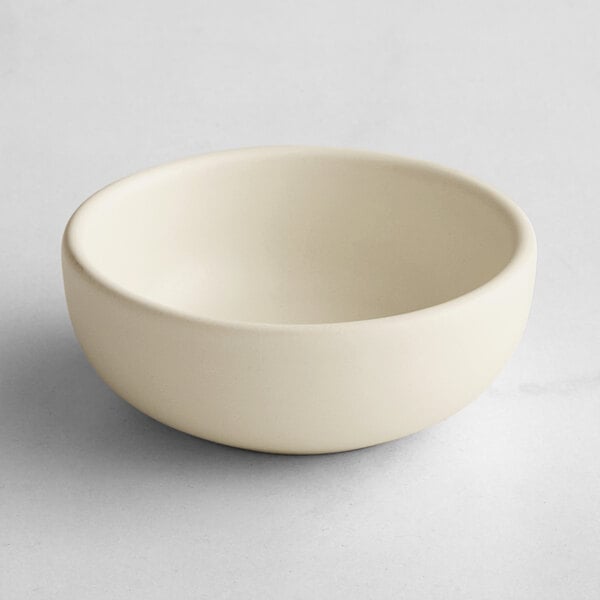 A small, round, matte white bowl with smooth sides and a simple design, placed on a light surface.