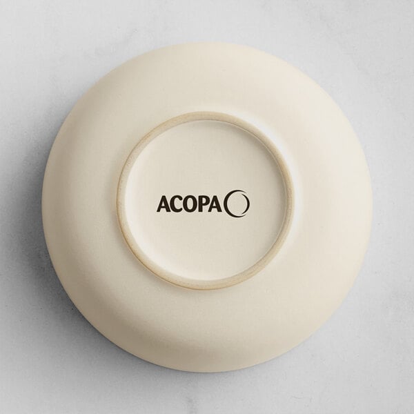 The image shows the underside of a small, round, off-white ceramic dish with the word 'ACOPA' printed in black on the base.
