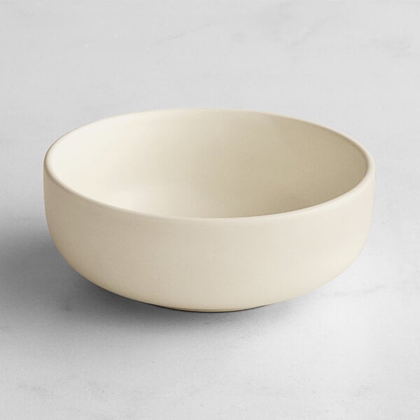 A simple, round, off-white bowl with a matte finish, placed on a light surface.