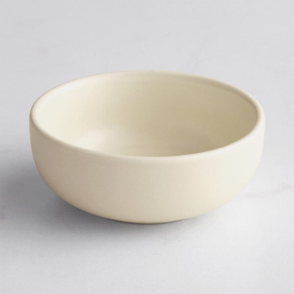 A small, round, off-white bowl with a matte finish is shown on a light surface.