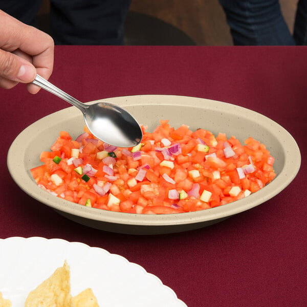 A person holding a spoon over a bowl of chopped tomatoes and onions.