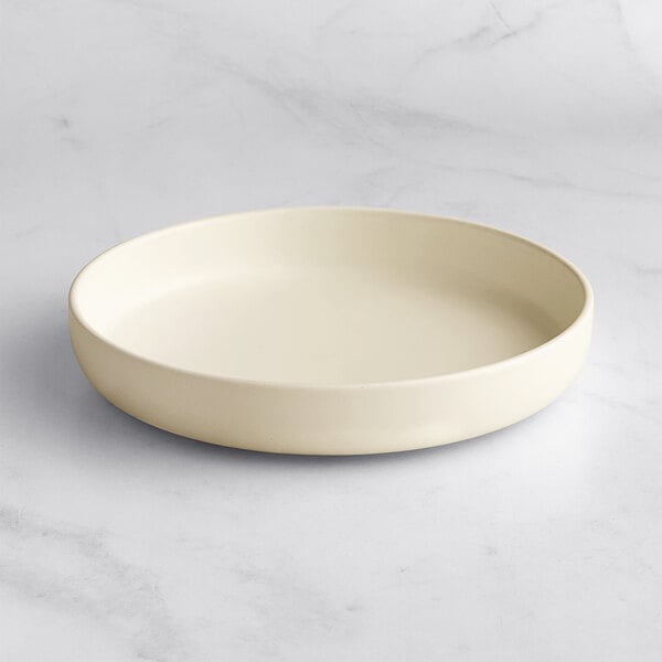 A round, shallow, off-white bowl with a matte finish, placed on a light marble surface.