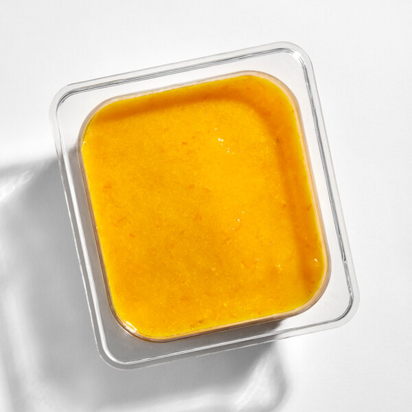 A clear square container filled with a bright orange-yellow, smooth and slightly textured paste or sauce.