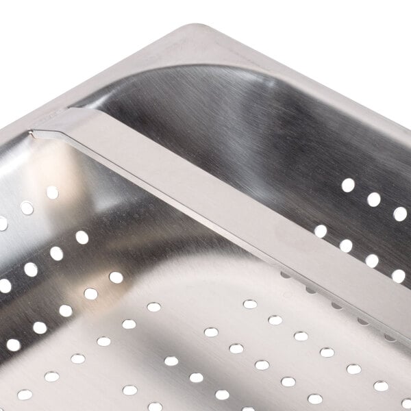 A stainless steel FMP pre-rinse basket with holes in it over a metal sink.