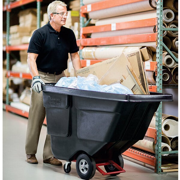 A man pushing a black Rubbermaid tilt truck cart full of garbage.