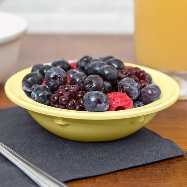 A yellow GET SuperMel bowl filled with cherries on a table.