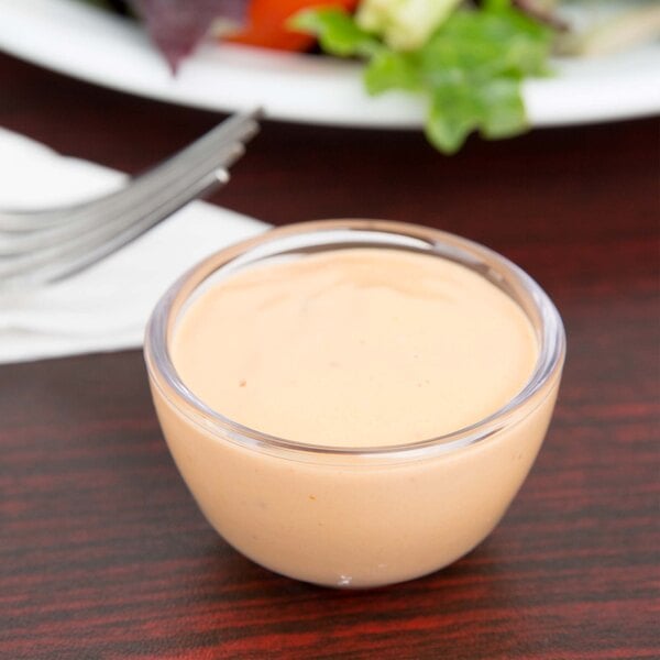 A clear Carlisle round plastic souffle cup filled with white sauce.