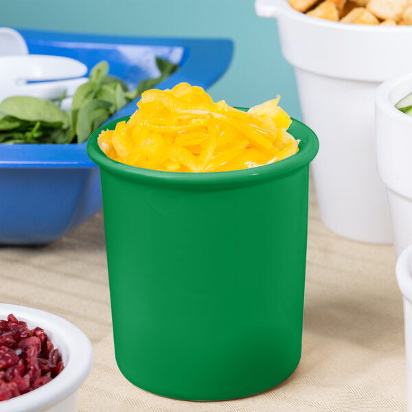 A green Tablecraft cast aluminum condiment bowl filled with yellow food on a table in front of bowls of food.