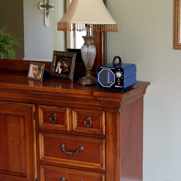 An OdorStop OS1200 ozone generator air purifier with a blue casing and control knob, placed on a wooden dresser.