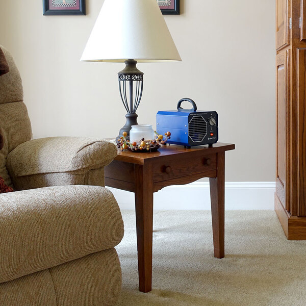 An OdorStop OS1200 ozone generator air purifier with a blue casing and handle, placed on a wooden side table in a living room.