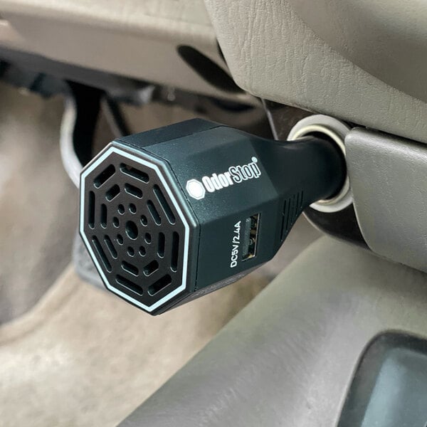 An OdorStop Ozone Go OSOGO ozone generator vehicle deodorizer with dual charging ports plugged into a car's power outlet.
