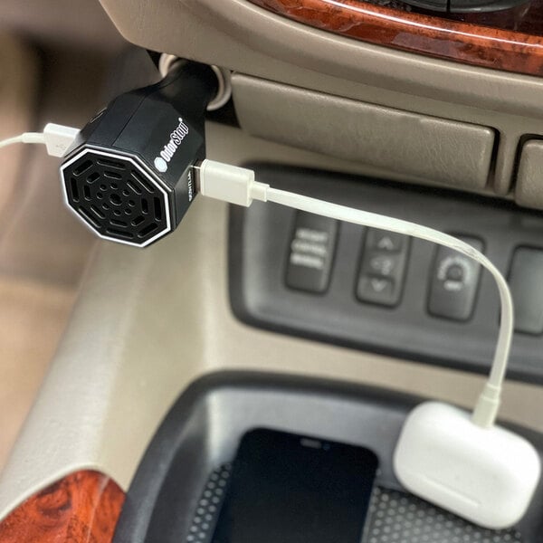 An OdorStop Ozone Go OSOGO ozone generator vehicle deodorizer with dual charging ports plugged into a car's power outlet.