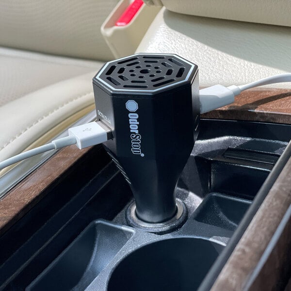 An OdorStop Ozone Go OSOGO ozone generator vehicle deodorizer with dual charging ports plugged into a car's power outlet.