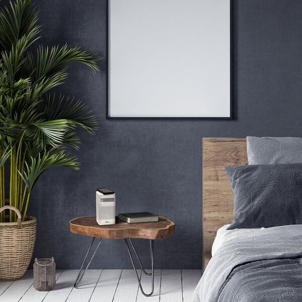 A white OdorStop OSAP2W HEPA air purifier with three speeds is placed on a wooden bedside table in a modern bedroom setting.