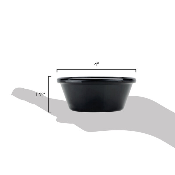 A hand holding a black Carlisle ramekin with measurements.