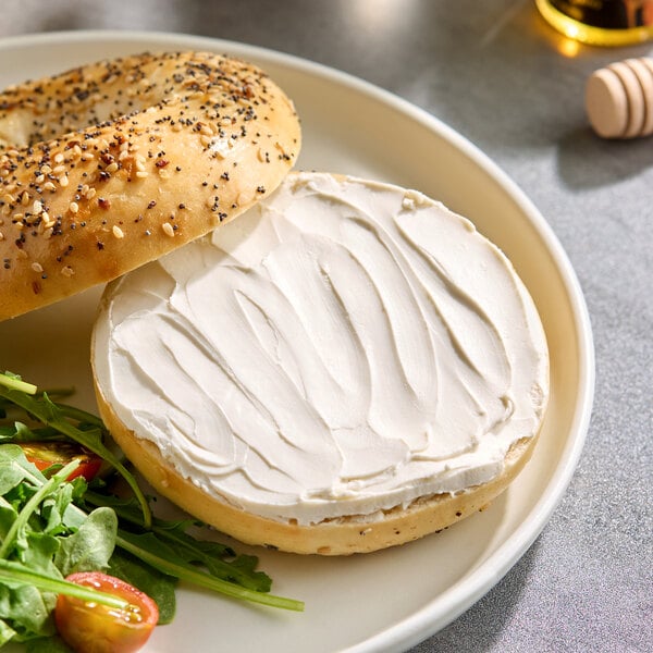 An everything bagel with vegan plant-based cream cheese served on a plate with a side salad.