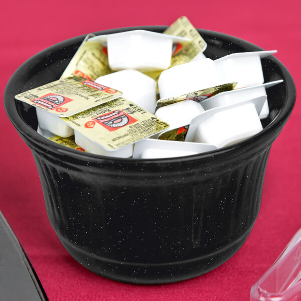 A black Tablecraft cast aluminum bowl with a spoon and a plastic bag of sugar.