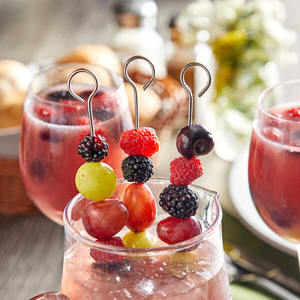 A set of stainless steel flat skewers used for holding assorted fruits, displayed in a beverage.