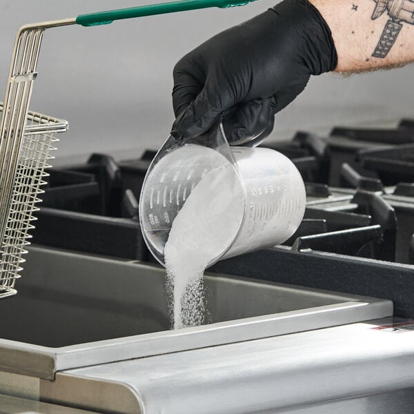 A person pouring a white powdered cleaner from a measuring cup into a deep fryer.