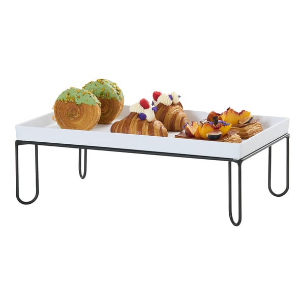 A rectangular black wire riser frame holding a white tray with assorted pastries on top.