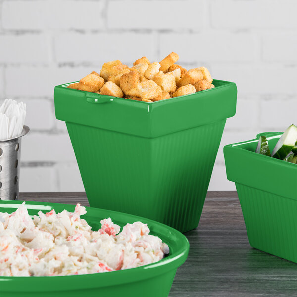 A group of green Tablecraft square condiment bowls with food in them on a counter.