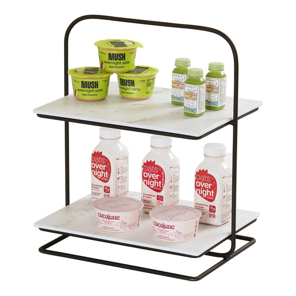 A two-tiered metal and marble display stand holding various packaged food and drink items.