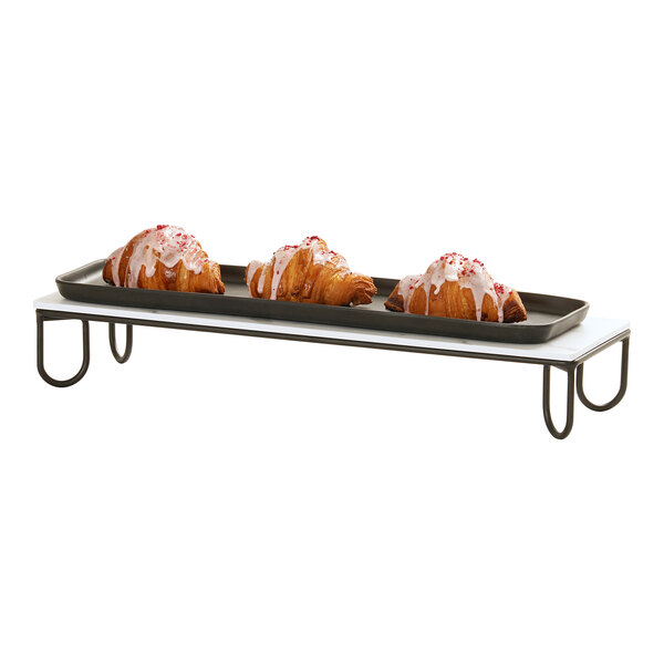 A rectangular black wire riser frame with a tray holding three iced croissants.