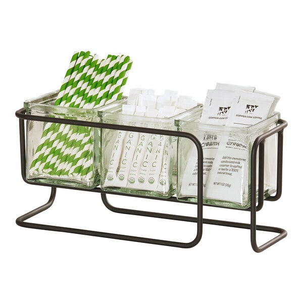 A three-jar display organizer holding straws, sweetener packets, and creamer packets in a metal frame.