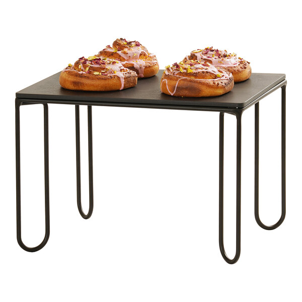 A black wire riser frame with a flat rectangular top, used for displaying items such as pastries.