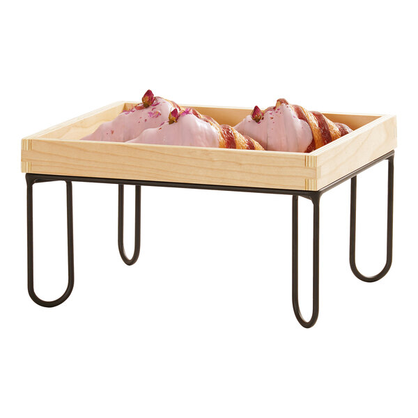 A rectangular wooden tray with a black wire riser frame, holding pastries with pink icing.