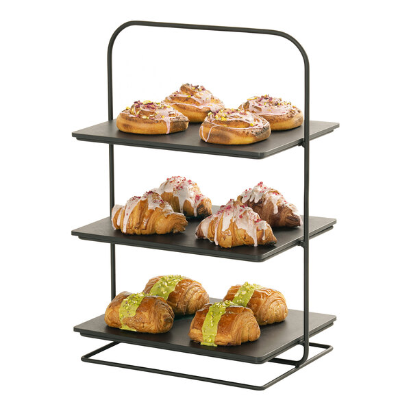 A three-tiered black metal display stand holding assorted pastries on each shelf.