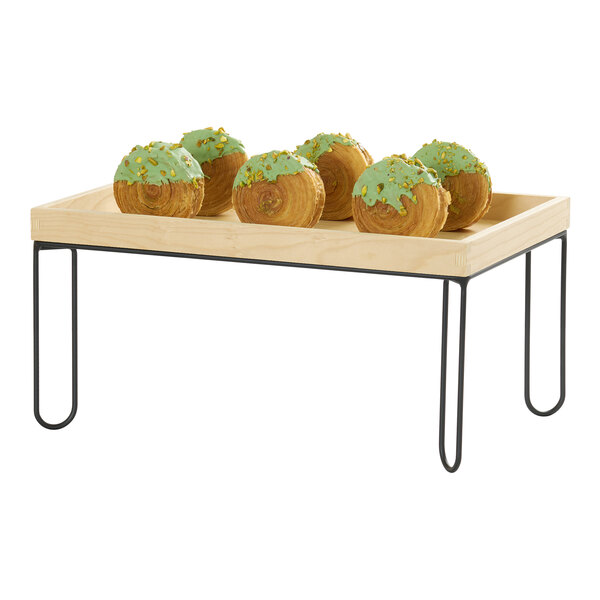 A rectangular wooden tray with a black wire riser frame, displaying pastries with green icing.
