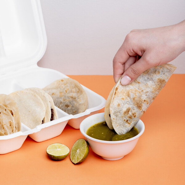 A white, compostable, three-compartment taco clamshell take-out container made from sugarcane fiber, shown holding several tacos.