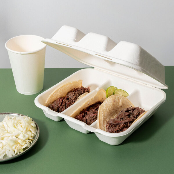 A compostable sugarcane fiber 3-compartment taco clamshell take-out container holding three tacos and lime wedges.