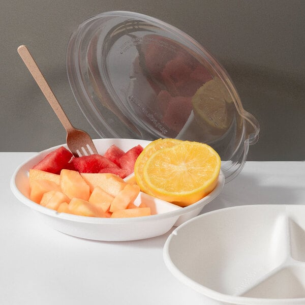 A round, white, 3-compartment compostable plate made from sugarcane fiber, shown with fruit and a clear plastic lid.