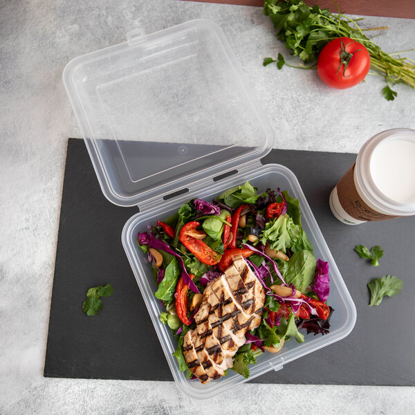 A clear, hinged, reusable take-out container filled with salad and grilled chicken.