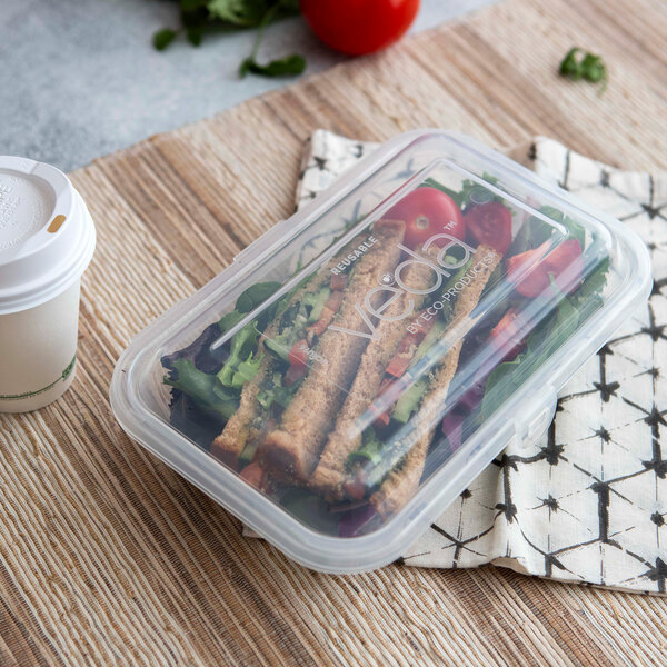 A clear hinged reusable take-out container filled with a sandwich and salad.