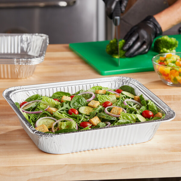 A deep, half-size light-duty foil steam table pan filled with salad, placed on a wooden countertop.