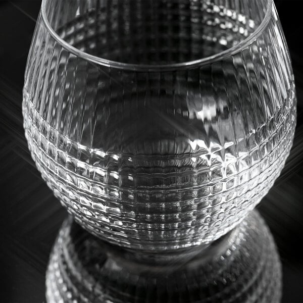 A clear, round glass with a textured, grid-like pattern on its surface, shown on a reflective black background.