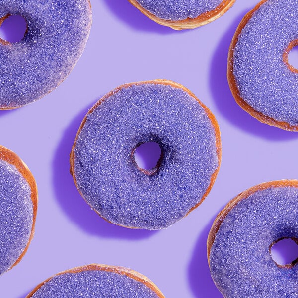 Several donuts topped with purple sanding sugar are arranged on a purple background.
