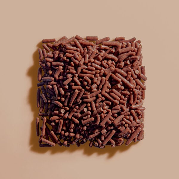A square pile of small, cylindrical, brown sprinkles arranged on a light beige surface.